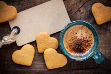 Valentine's Day background with copyspace. Romantic morning with cup of espresso coffee, heart shape cookies and an empty tag on rustic wooden table