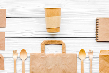 Set of recycle brown paper bag, disposable tableware cup, spoon, fork, notebook on white wooden background top view pattern copyspace