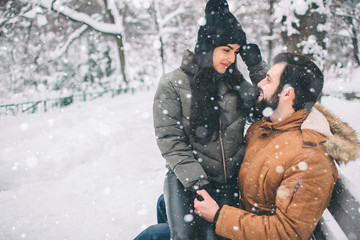 Happy Young Couple in Winter . Family Outdoors. man and woman looking upwards and laughing. Love, fun, season and people - walking in winter park. Female model sits on his lap.