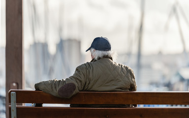 Jubilado sentado en un banco del puerto al sol al atardecer