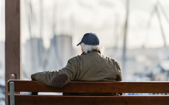 Jubilado sentado en un banco del puerto al sol al atardecer