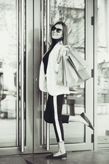 Happy young woman with shopping bags entering shop. Happy woman going into a store. Black and white photo