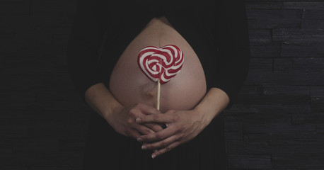 Mujer muestra una piruleta roja y blanca delante de su barriga de embarazada