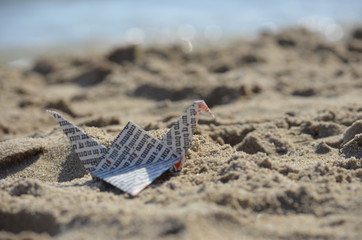 Grulla de papel apoyada en la arena donde se ve el mar a lo lejos