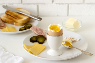 Breakfast with soft-boiled egg, bread toast, ham, cheese and canned cucumbers. Rustic style.