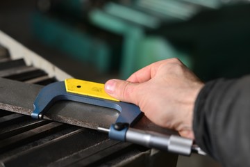 Elderly worker looks in the drawing to see detail sizes. The man turner measures the dimensions of the part on a micrometer, and also uses a sliding caliper.