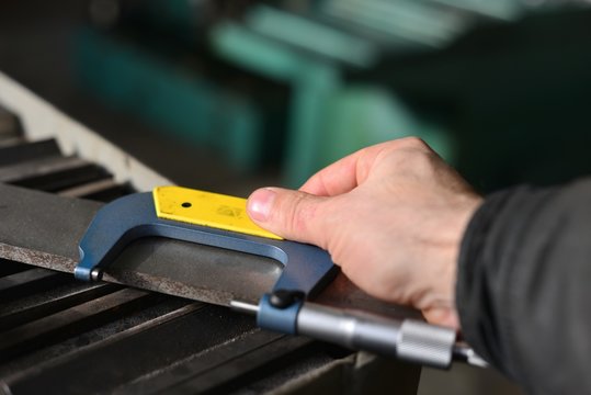Elderly worker looks in the drawing to see detail sizes. The man turner measures the dimensions of the part on a micrometer, and also uses a sliding caliper.