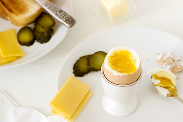 Breakfast with soft-boiled egg, bread toast, ham, cheese and canned cucumbers. Rustic style.