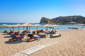 Fototapeta na wymiar Stegna beach with sunshades and sunbeds, boats in background (RHODES, GREECE)