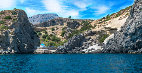 Fototapeta premium Hidden white and blue chapel near sea under cliff, (RHODES, GREECE)