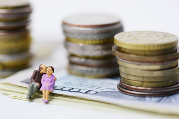 Aged couple sitting on a bench having behind a jar full of money or coins
