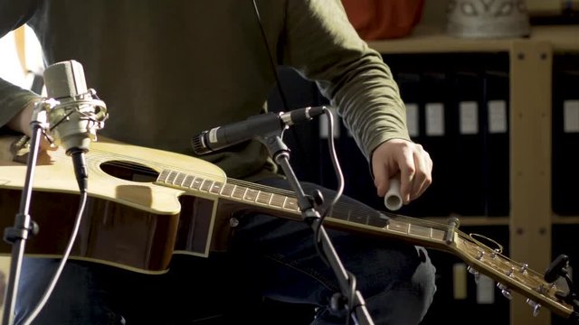 Tight camera slide to left of man playing slide guitar with microphones for a performance.