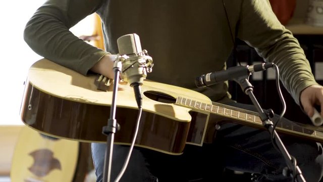 Tight camera slide to right of man playing slide guitar with microphones for a performance.