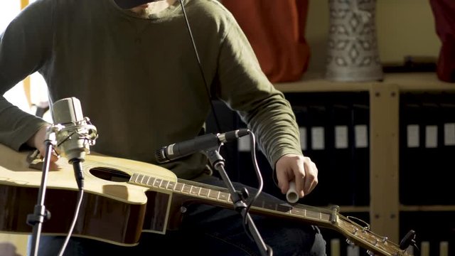 Medium tight camera slide to right of man playing slide guitar with microphones for a performance.