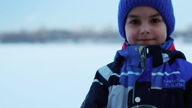 Close up of little boy drinking tea from termo cup in winter. Winter child with hot drink. Boy face with termos. Winter holiday rest