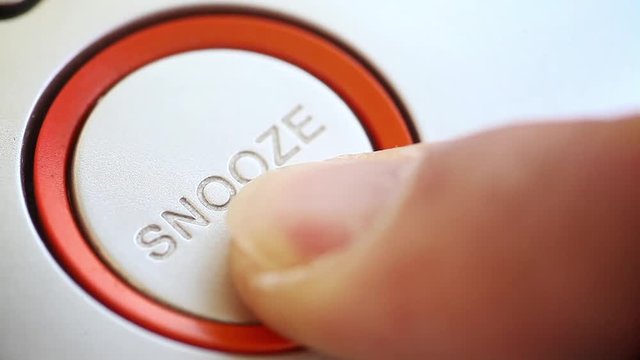 Person pushing the snooze button on an alarm clock.