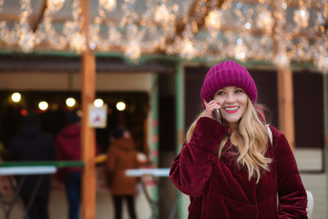 Merry young woman talking on the mobile phone at the background of christmas lights