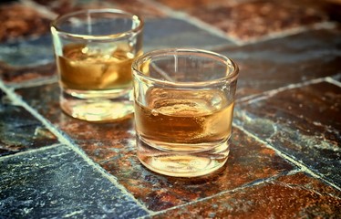 Alcohol,taste and drink concep-two glasses of whisky on a old stone background.