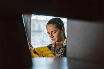 there is a profile of beautiful slim girl with dark hair, a round face and pouting lips which reads a book sits near window