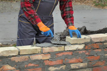 Worker building brick wall using trowel tool for mortar spreading