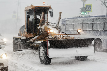 Snow plow truck removes snow from road during heavy snow winter storm, poor visibility
