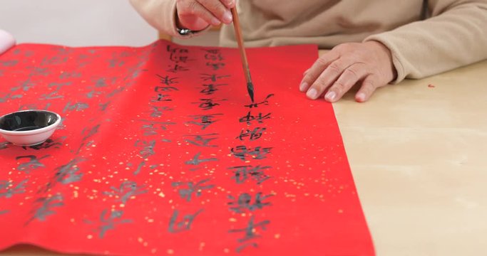 Asian man writing chinese calligraphy on red paper