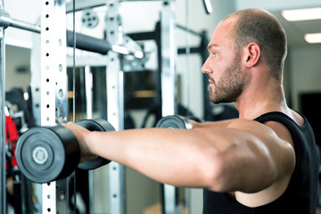 Junger Bodybuilder trainiert im Fitnessstudio seine Muskeln mit Kurzhanteln, am Kabelzug und macht Klimmzüge. Bizeps, Trizeps, Latissimus
