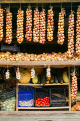 Vegetables market wooden racks full of different products. Large onion bundles hanging. 