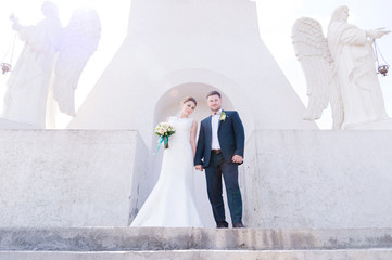 Portrait of a lovely couple honeymooned on a wedding day with a bouquet in hand against the background of an Orthodox Christian monument with angels.