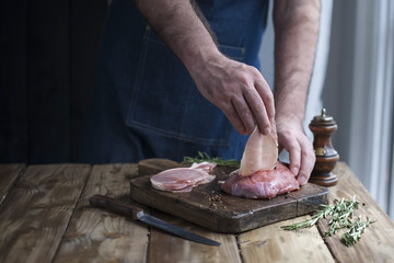 man in kitchen apron holds meat in hands, wooden table and spices