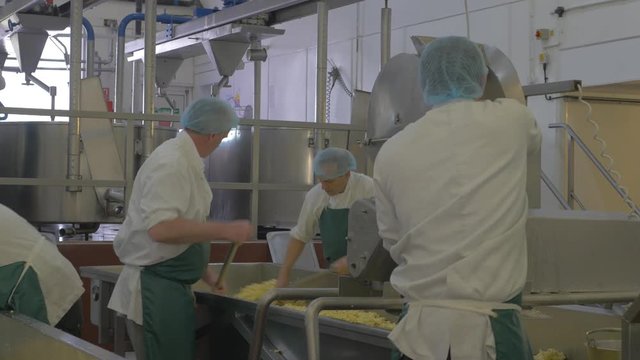Employees using mahine to mill fresh cheese in factory