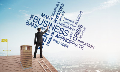 Young businessman standing on house roof and writing leadership skill concept. Mixed media