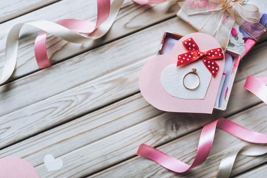 A gift for Valentine's Day. A wedding ring on a gift box with ribbons and hearts on a wooden background. Festive decor. View from above. Copy space.