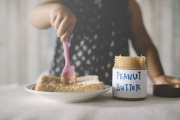 Asian Baby girl playing / spreading peanut butter on a bread. Baby making a mess with peanut butter