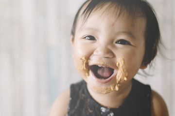 Asian Baby girl smiling with mouth and face full of peanut butter