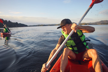 Kayaking man at the kayak boat getting leisure on the lake in evening time