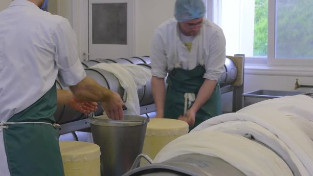 Two cheese factory employees add a special cloth to the cheese to help with the processing