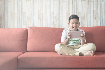 young asian boy using digital tablet on a sofa at home sitting cross-legged. boy relaxing on sofa at home. technology / IT concept. Computer learning concept .