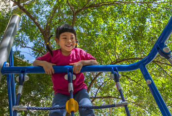 Adorable little Asian girl enjoying her time in climbing adventure park in sunny day. Little Asian girl having fun at school playground. Worm eyes view image.