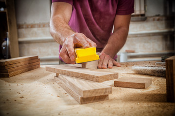 Close-up of a young strong male carpenter builder in a purple working football polishes a wooden...