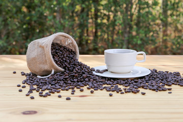 Hot coffee in a white porcelain cup with roasted coffee bean on the wooden desk with bokeh background