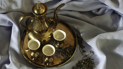 Fototapeta na wymiar Tea pot of gold. Put on a blue cloth and tea leaves. The smoke of steam, hot tea.
