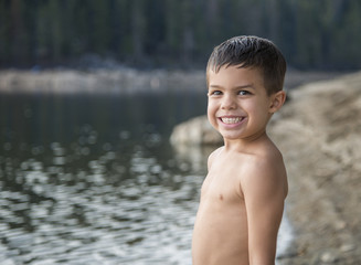 Cute, shirtless, little boy smiling at edge of mountain lake