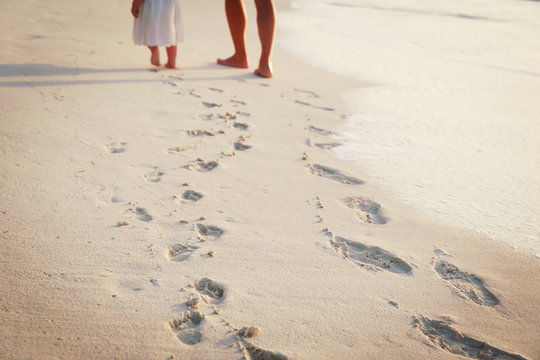 mother and daughter walking on beach leaving footprint in sand