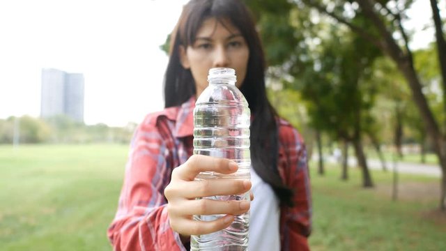 Asian woman drinking water at park. 