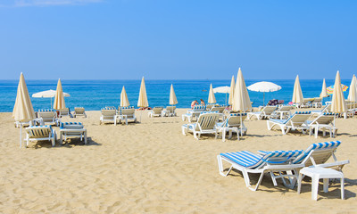Luxury resort beach with umbrellas and sun beds on white sand near blue sea on bright sunny day. Tropical beach with tourists. Summer vacation concept.