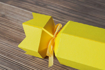 A part of Christmas or holiday yellow present box in the form of candy from multi-colored cardboard on wooden background. Selective focus