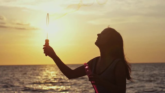 Pretty happy woman blowing soap bubbles on the beach at sunset in slow motion with sea view. 1920x1080