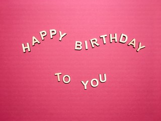 Fototapeta na wymiar Happy birthday to you made of wooden letters with a wooden floral frame on a pink background