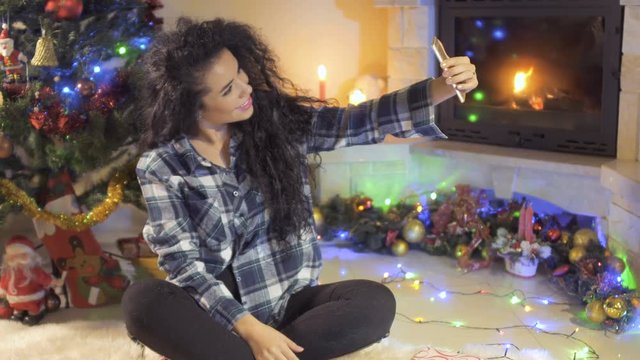 Beautiful curly brunette makes a selfie at Christmas tree background